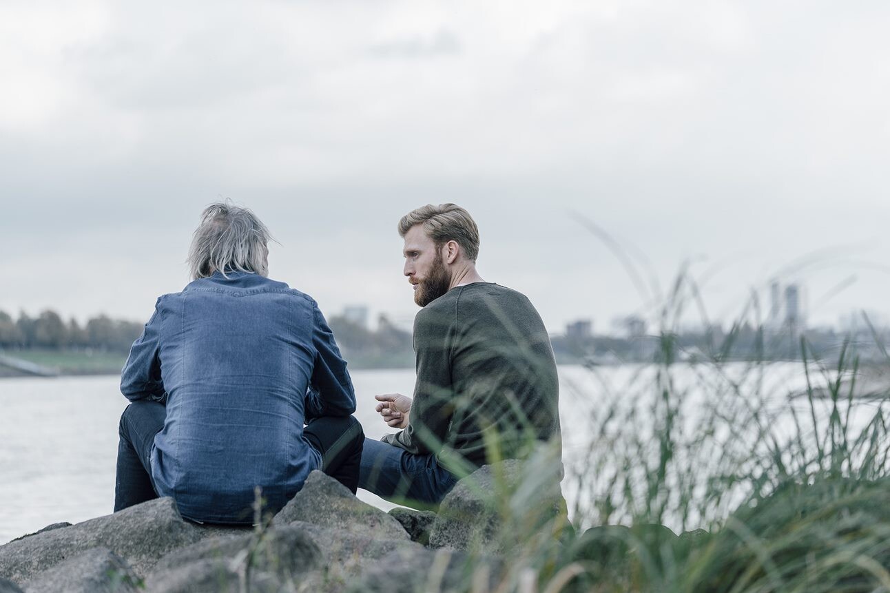 Vater und Sohn im Gespraech an einem Fluss