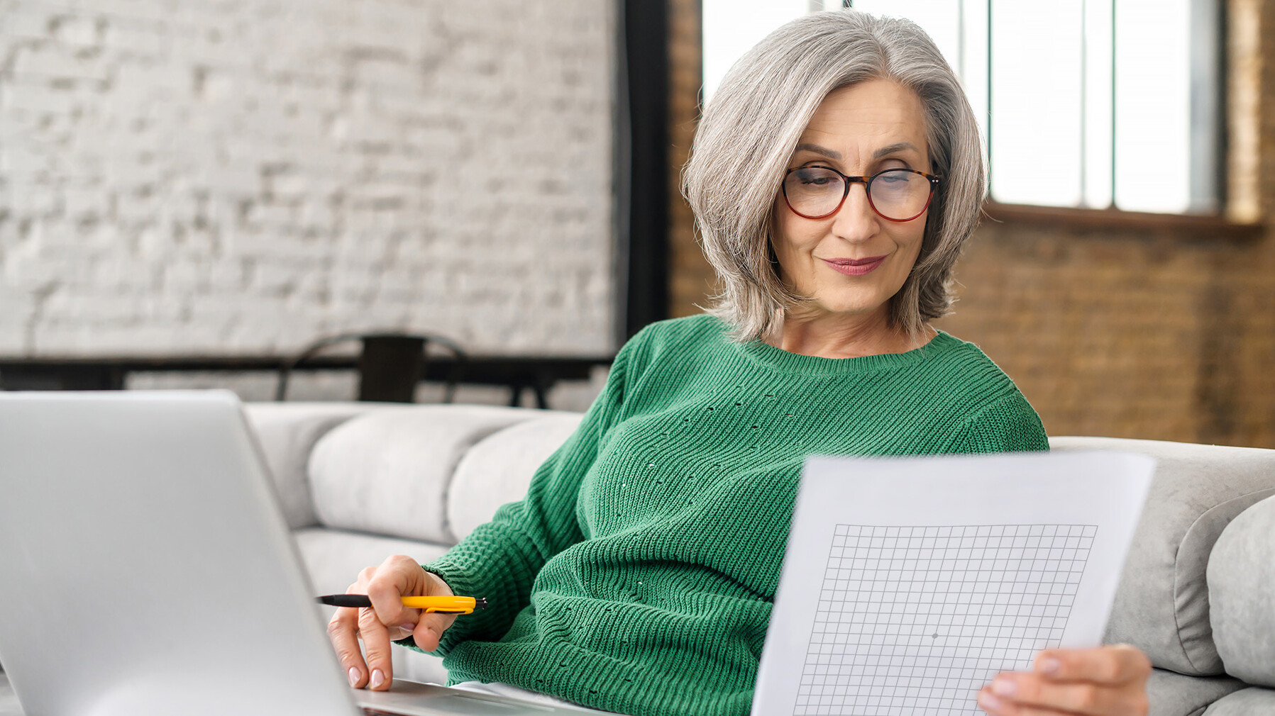 Frau mittleren Alters sitz mit Laptop auf der Couch und macht den Amsler-Gitter-Test