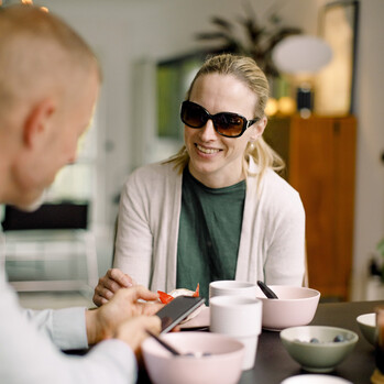 Frau mittleren Alters mit dunkler Brille drinnen beim Frühstück