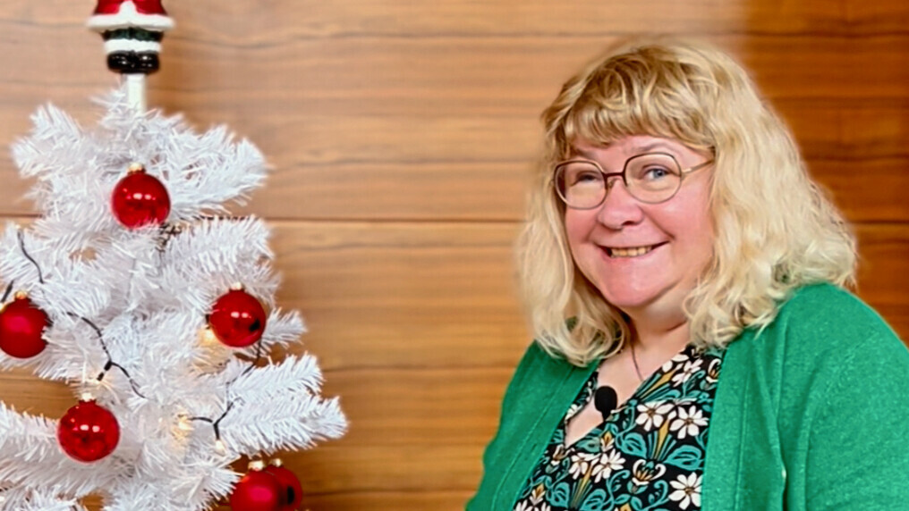 Eine Frau steht mit einer grünen Weihnachtskugel in der Hand vor einem weißen geschmückten plastik Weihnachtsbaum