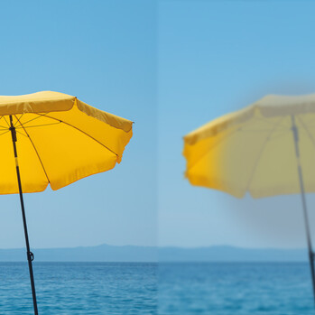 Gelber Sonnenschirm vor blauem Meer + Himmel, einmal scharf und einmal unscharf