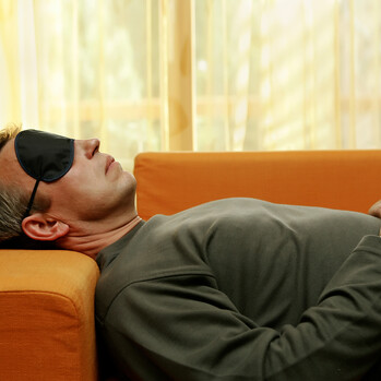Mann mittleren Alters liegt mit Augenmaske auf der Couch