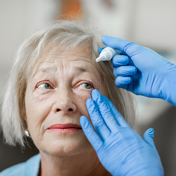 Medizinische Fachkraft träufelt Augentropfen in die Augen einer älteren Dame