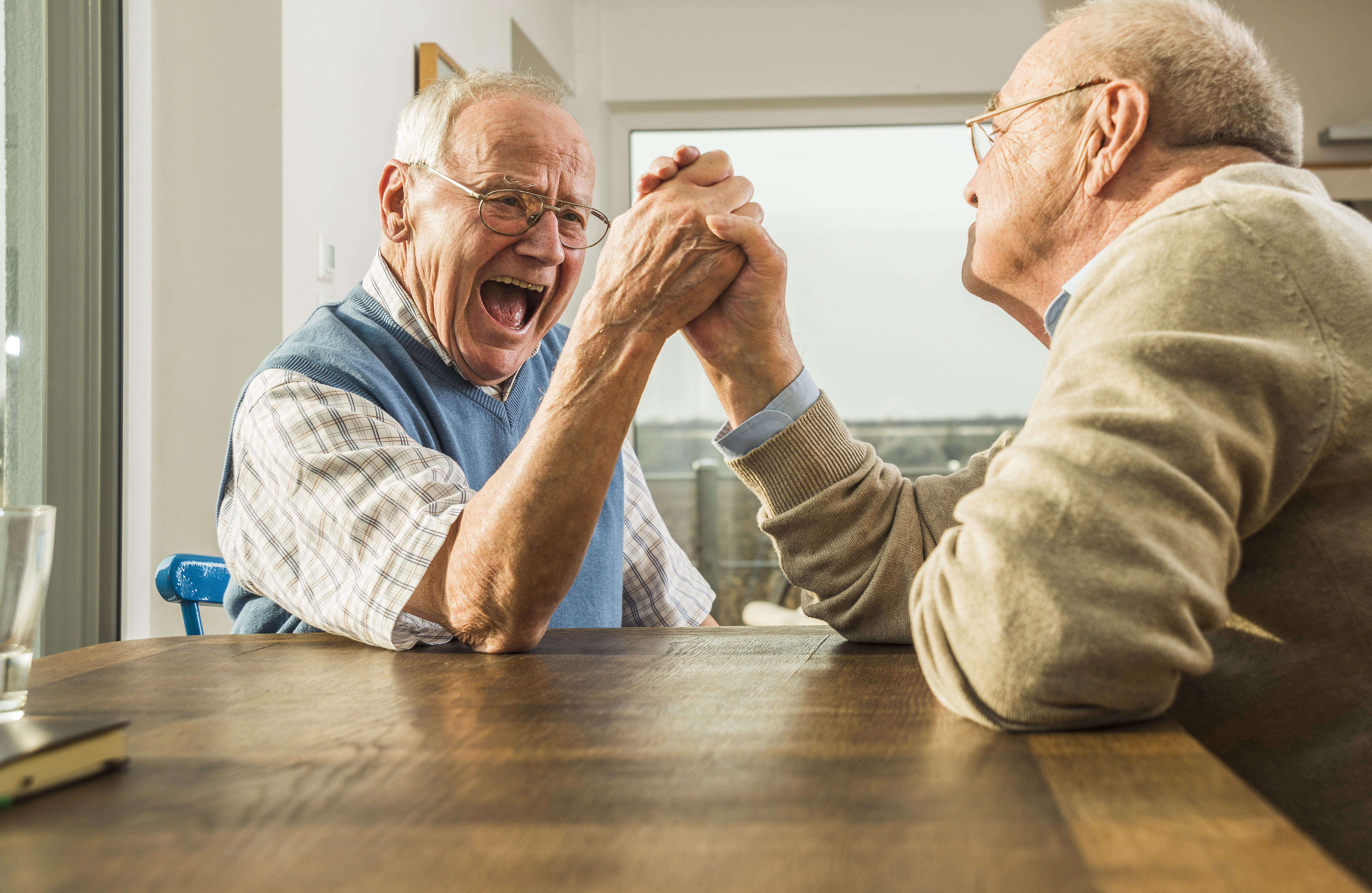 Zwei ältere Männer spielen Armdrücken und lachen sich an